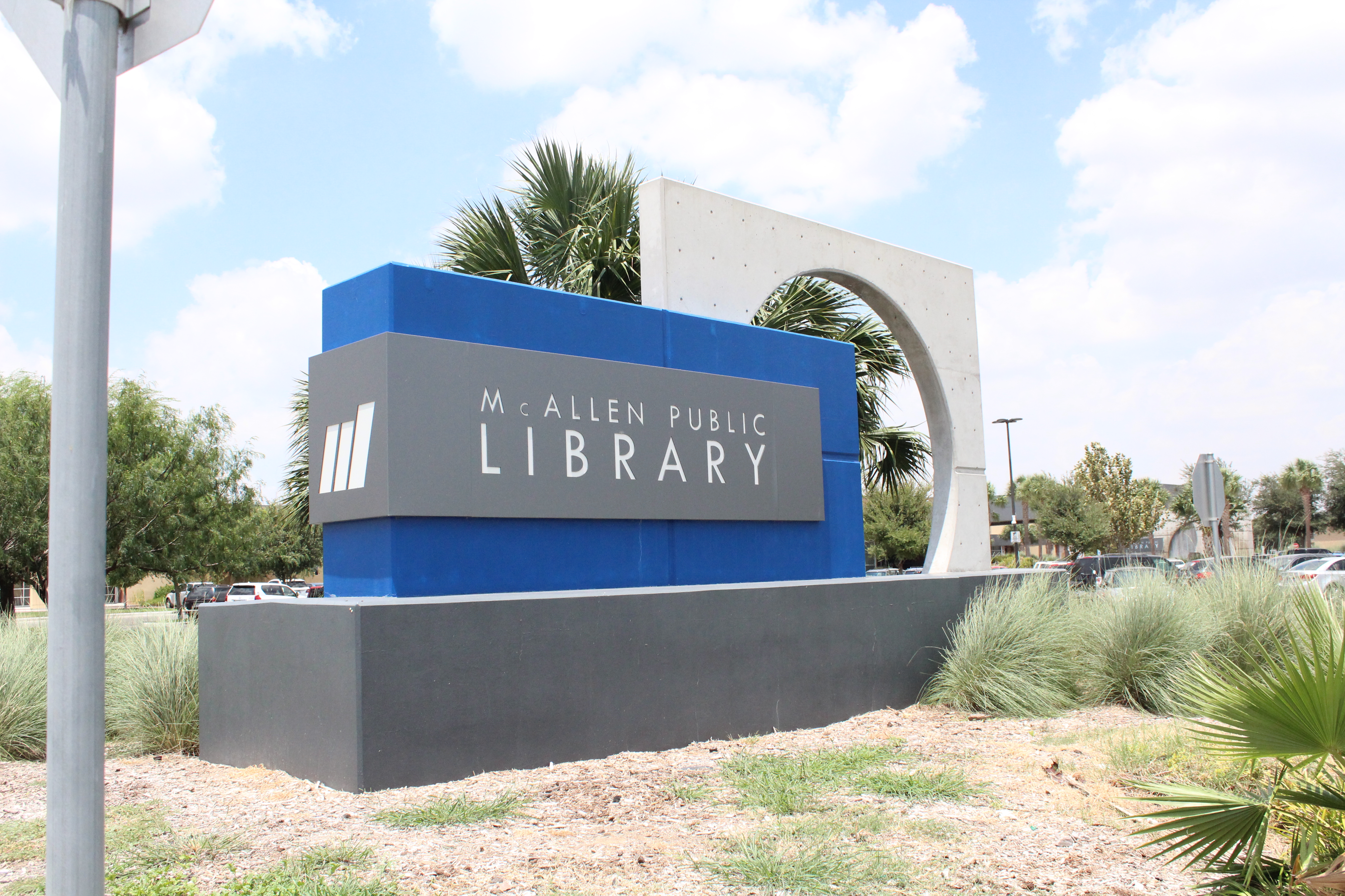 McAllen Public Library sign outside the Main Library building with landscaping and palm trees.
